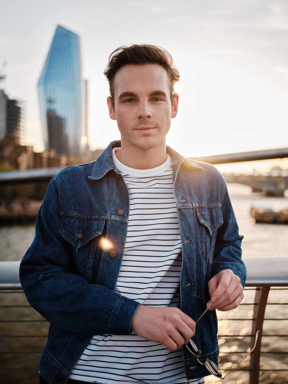 Man standing in a denim jacket with city skyline lights in the background
