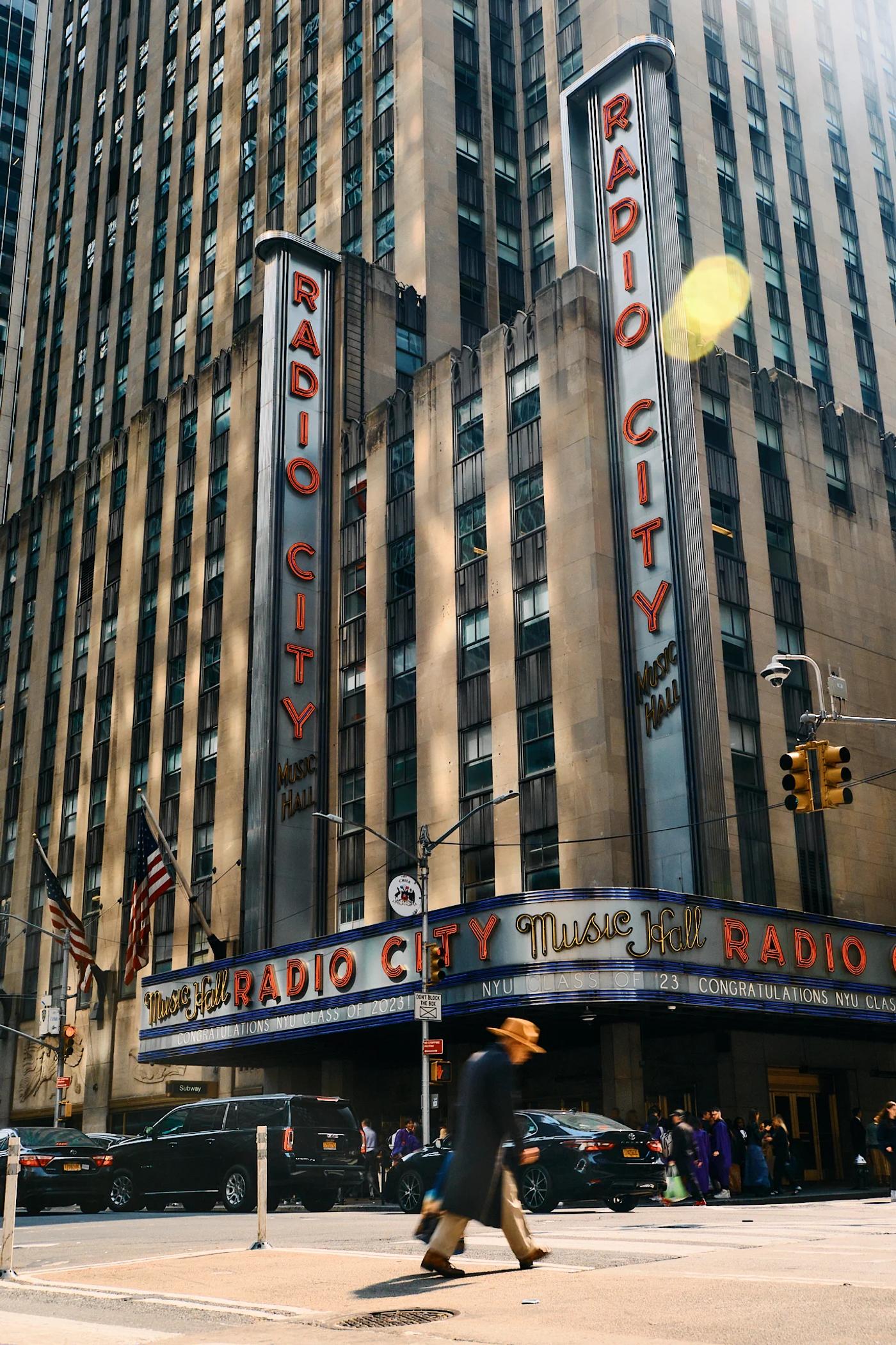 The image captures the iconic Radio City in New York City, featuring the iconic Radio City sign, two towering pillars, and a bustling street scene. Th