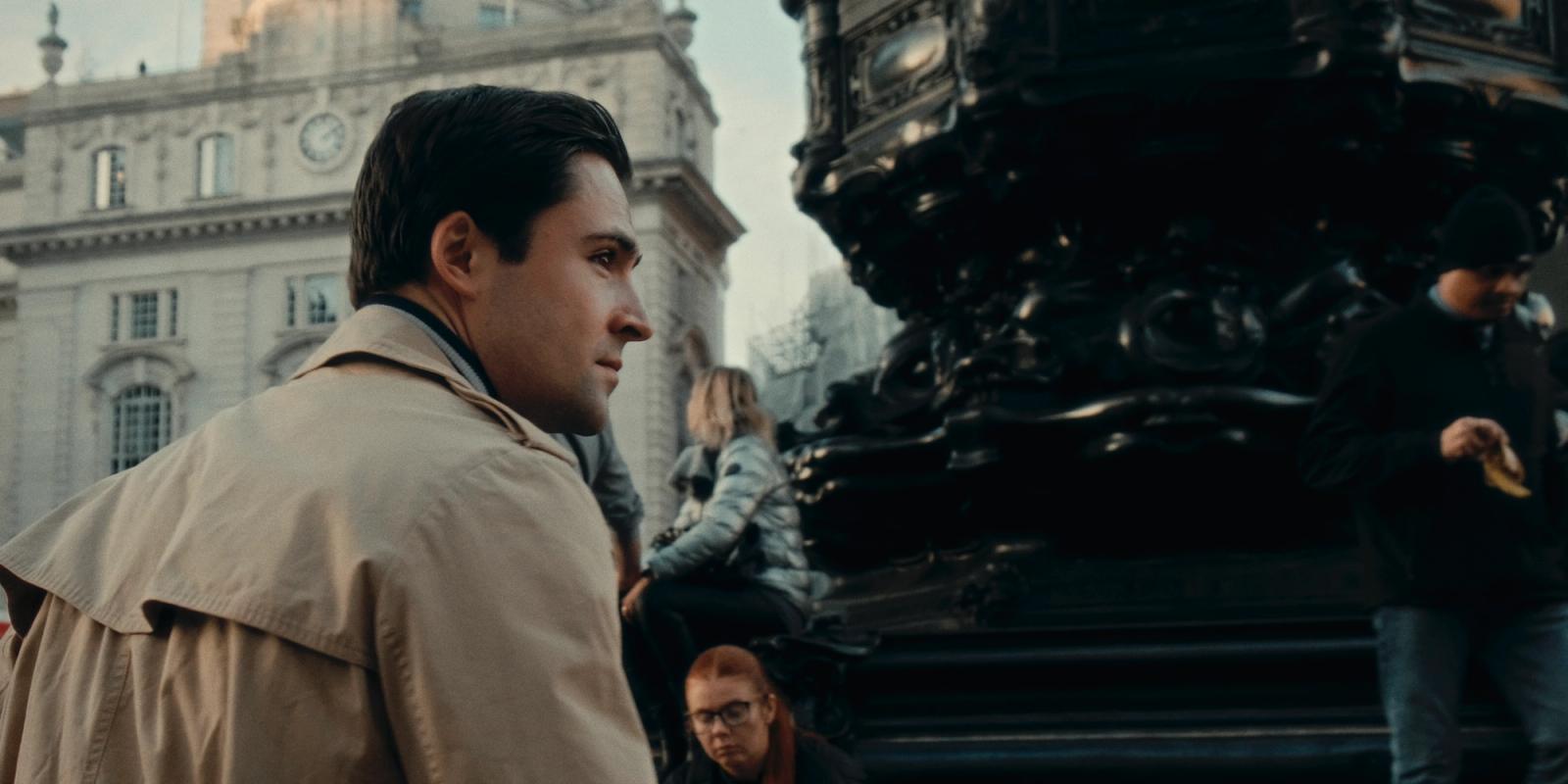 Maxim Gennett, known for his role as the lead character of "The Great Gatsby," is captured in a moment of contemplation on a city street. He is dresse