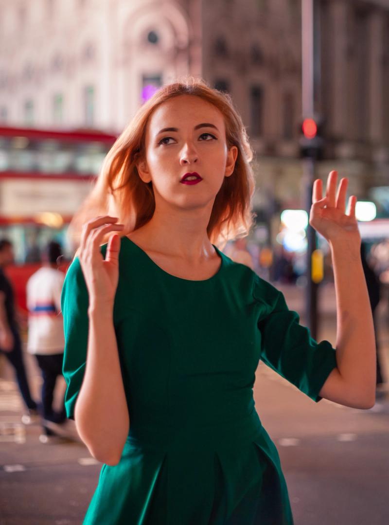Portrait of a woman in a green dress with colorful city lights behind her