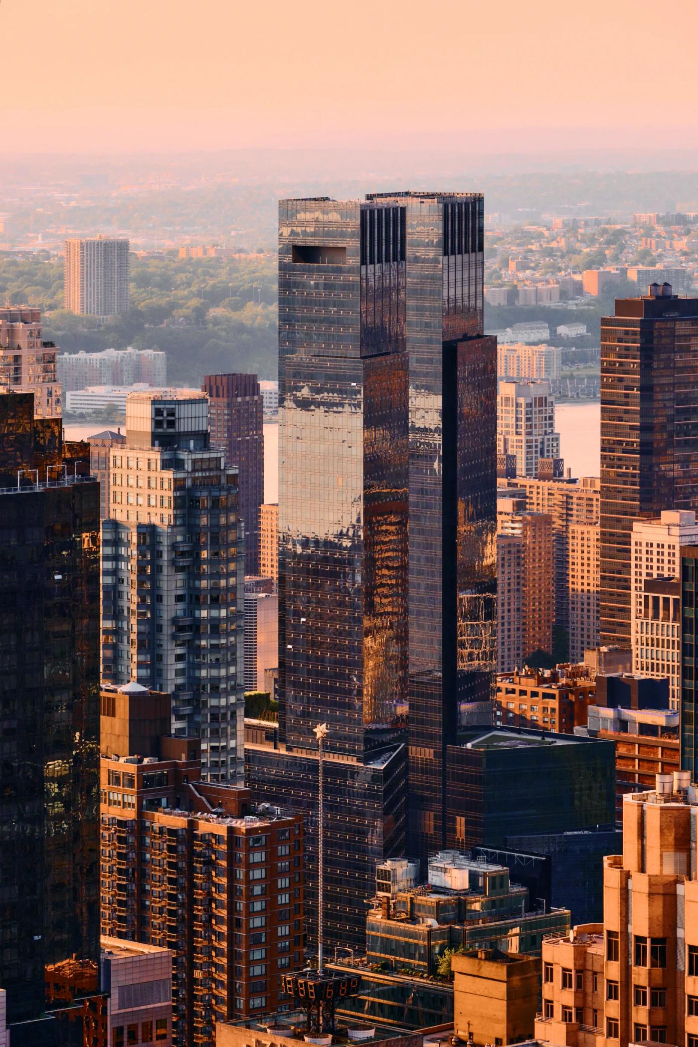 A bustling cityscape with tall buildings, reflecting the sunset, is captured from a high vantage point.