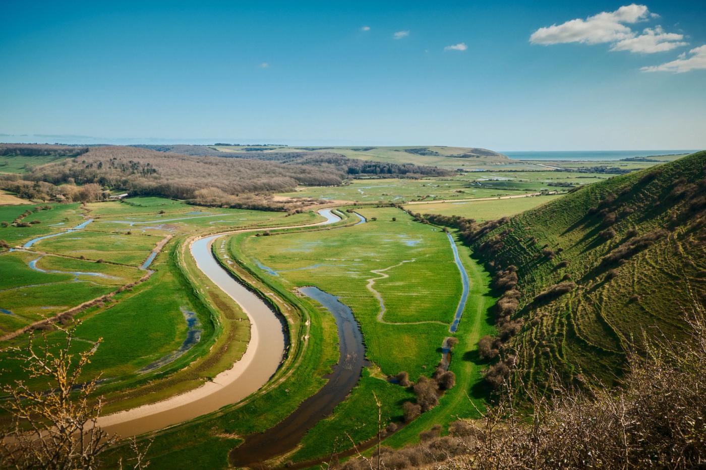 A serene landscape features a winding river, lush green hills, and a clear blue sky.