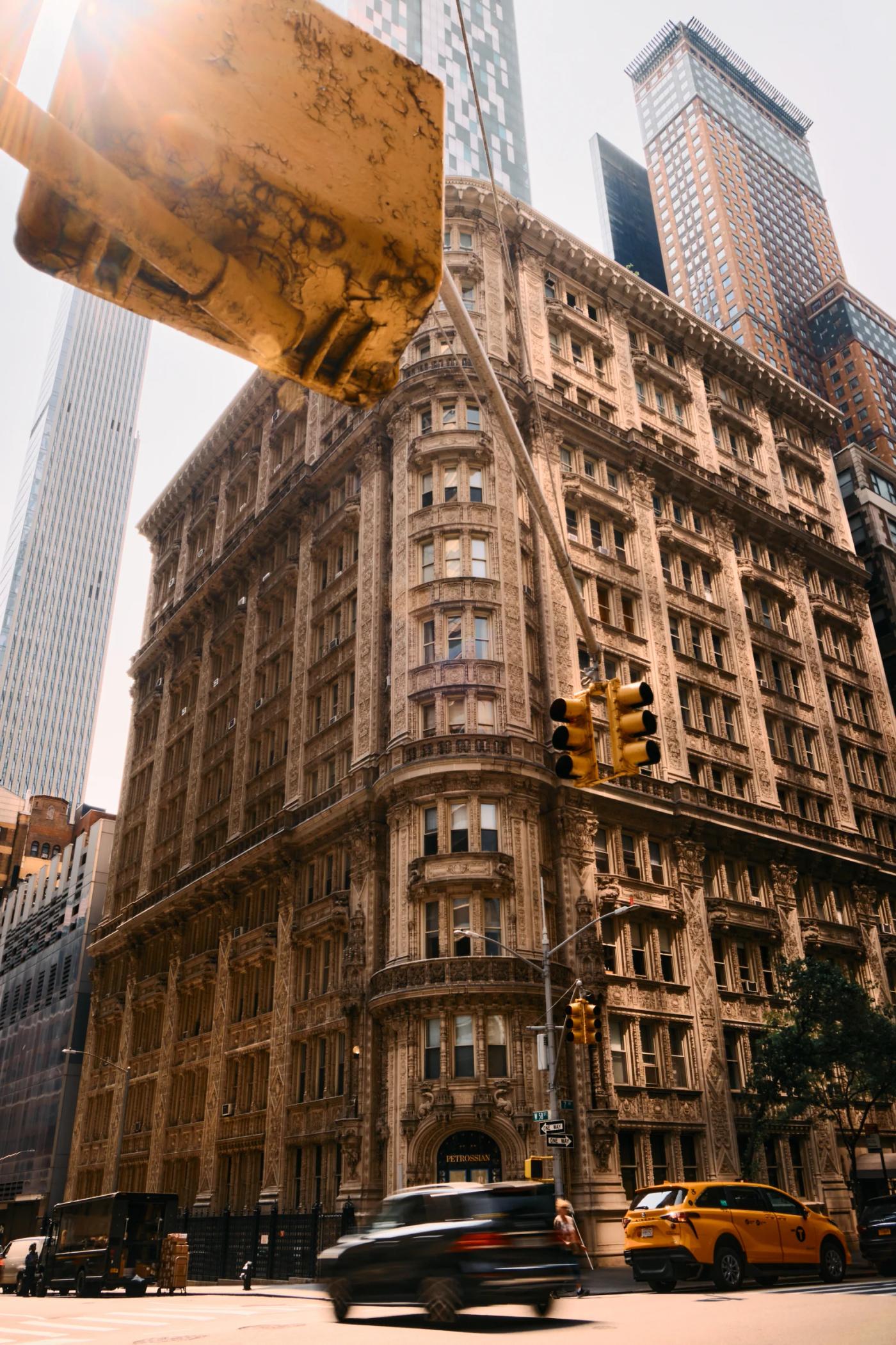 A bustling city street with tall buildings, parked cars, and a yellow taxi.