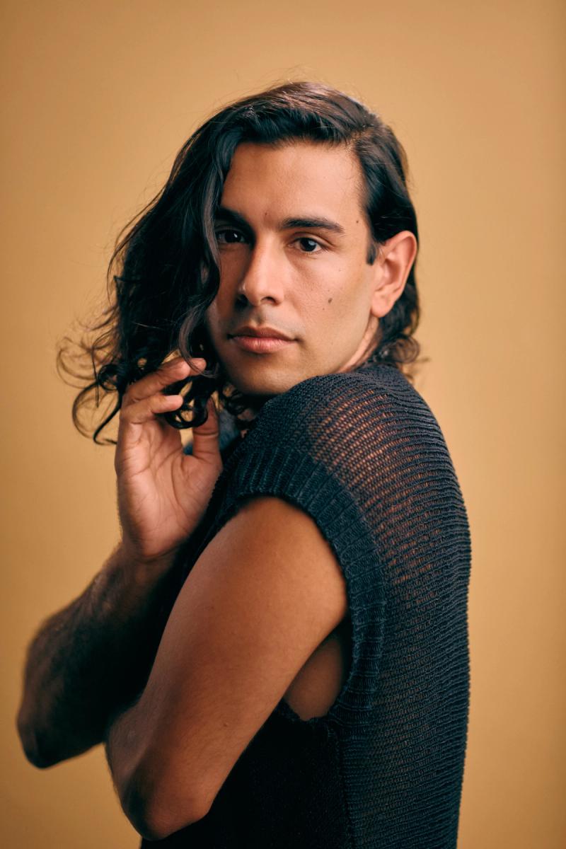 Close portrait of a young man in black on a warm neutral background