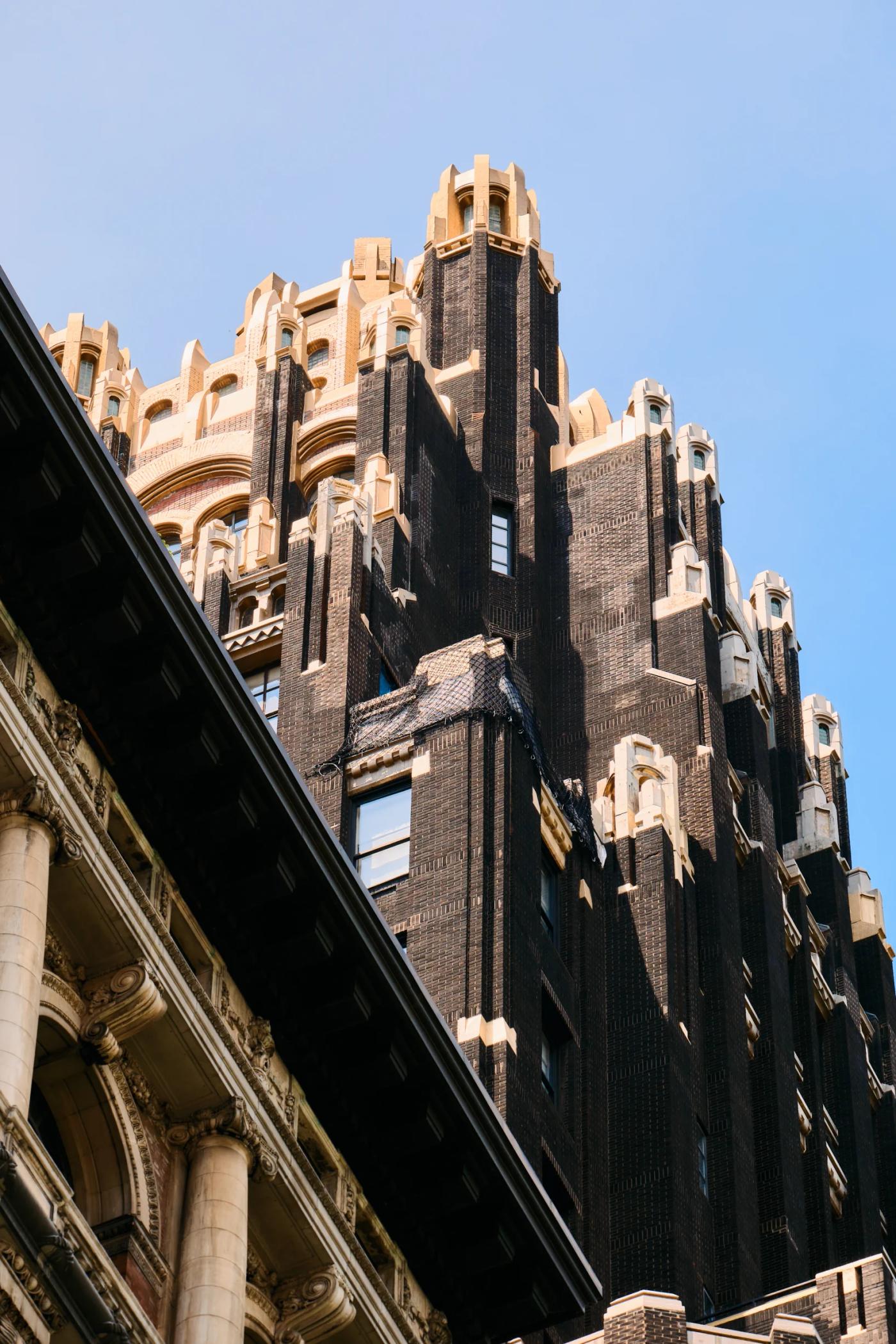 A tall, dark-colored building with ornate details and a pointed roof stands against a clear blue sky.