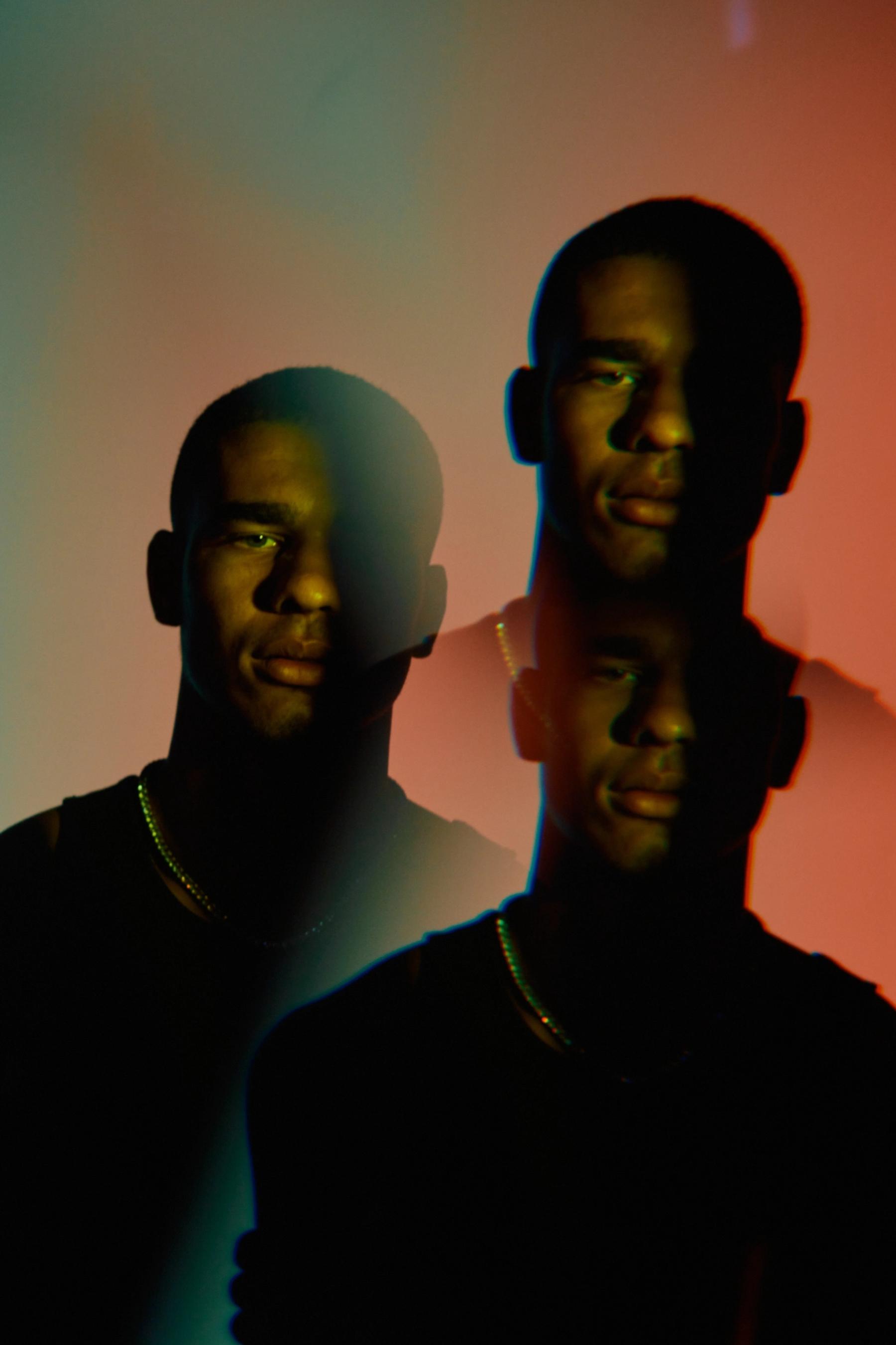 Two men in black shirts, one on the left and one on the right, with a colorful background.