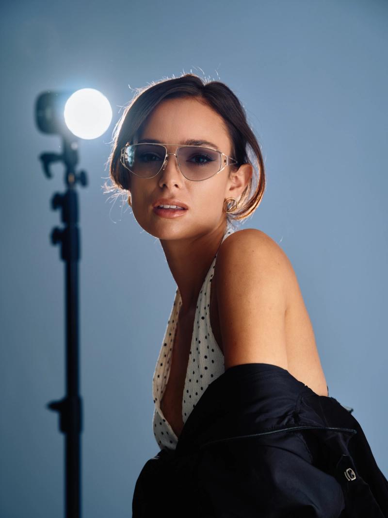 Fashion portrait of a woman in sunglasses and a white halter top against a blue backdrop