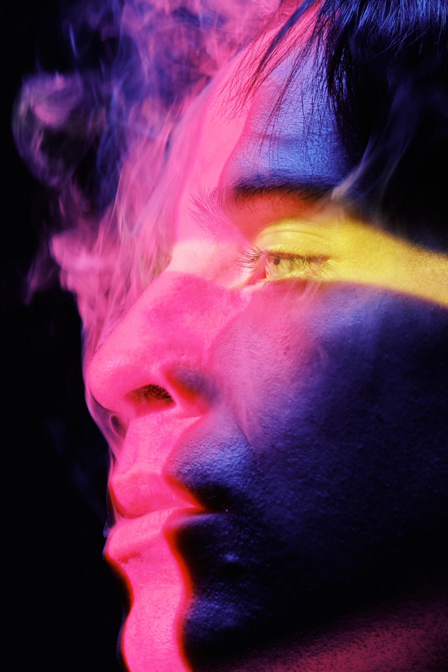 A close-up of a man's face, with a pink and purple glow, his eyes closed, and a yellow nose.
