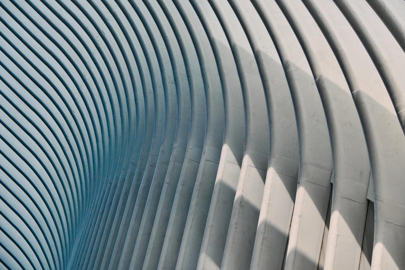 A modern, white, curved structure with a light blue sky background, showcasing a blend of modern architecture and natural beauty.