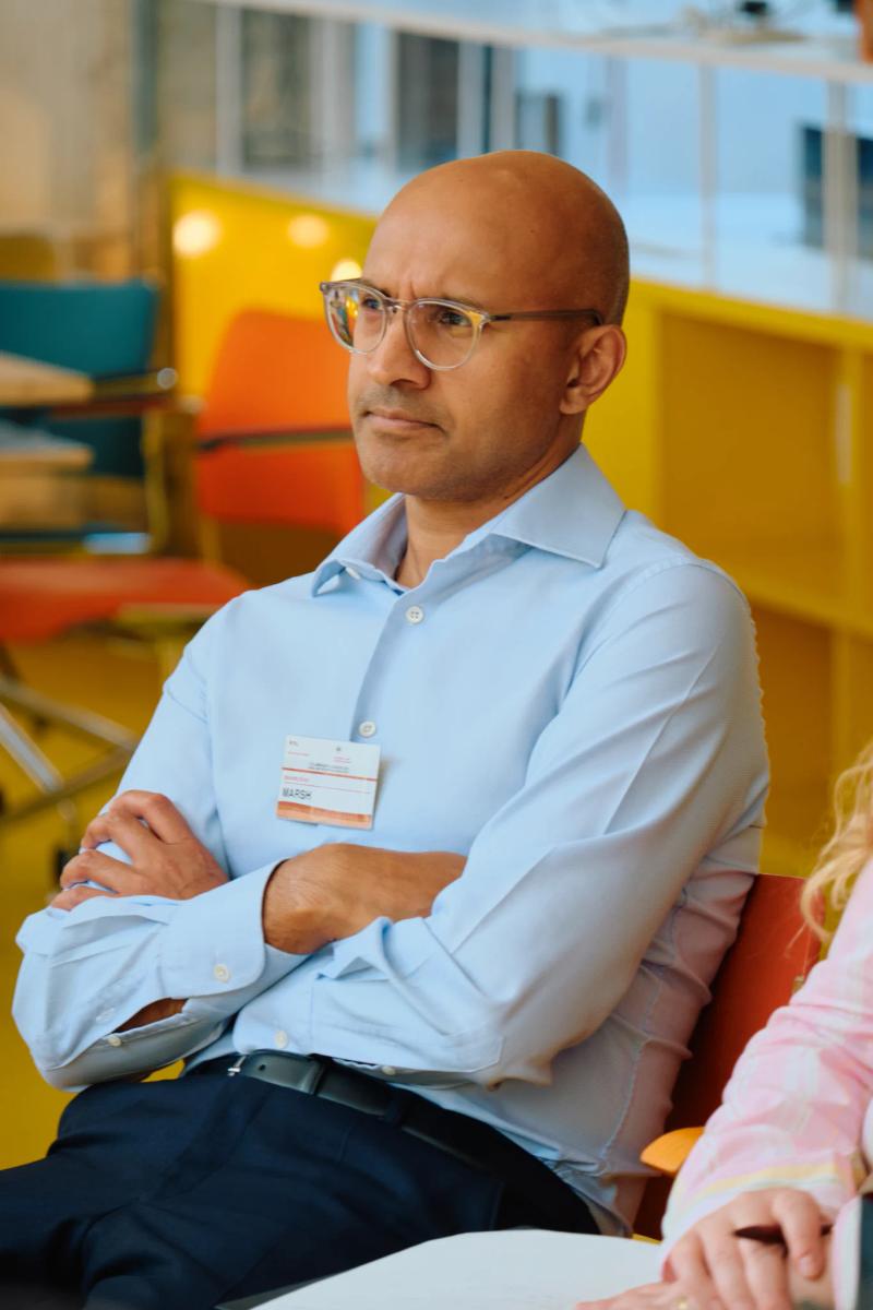 A man with glasses and a blue shirt is sitting in a chair.
