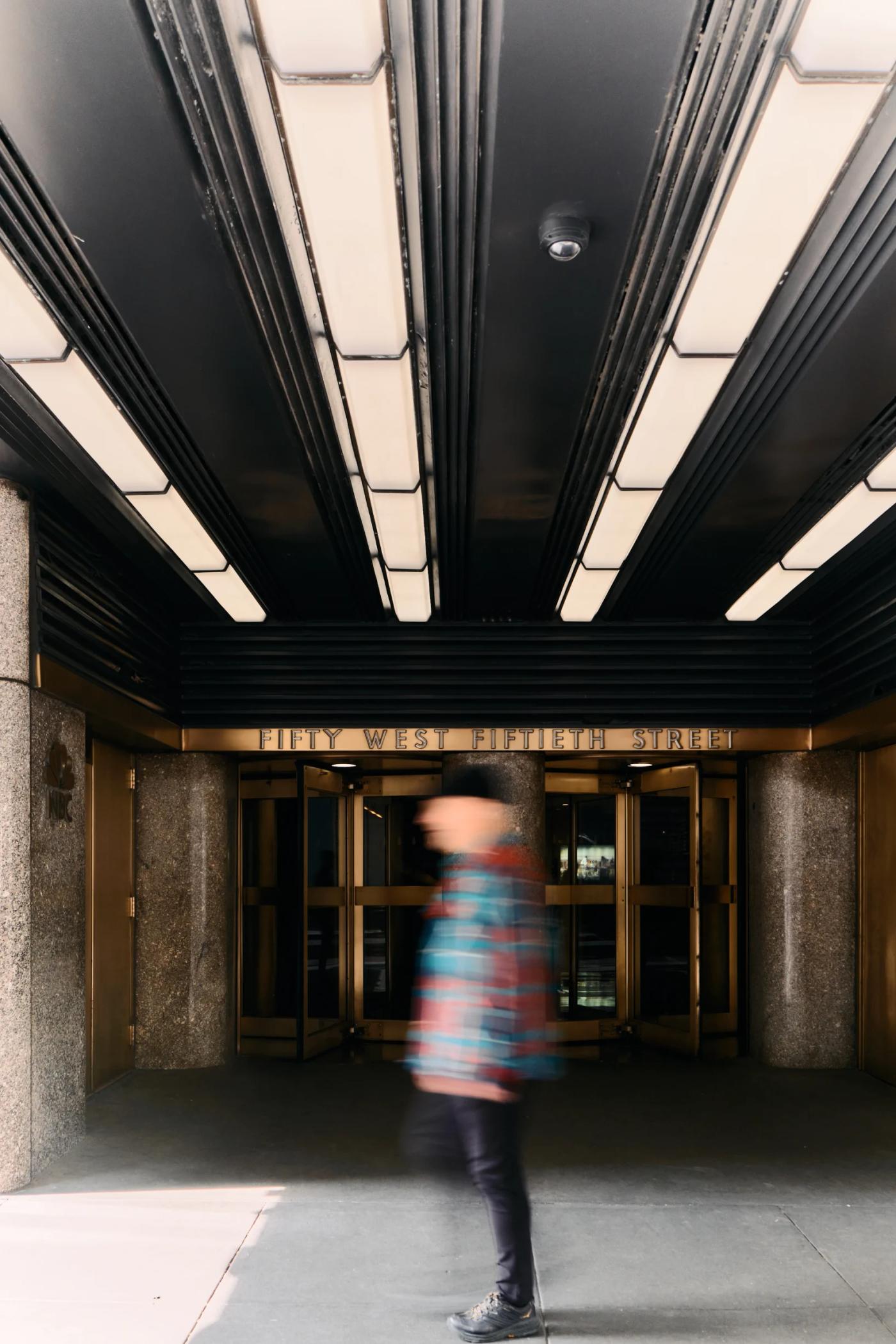 A blurred person walks through a grand entrance, with a black ceiling and gold doors.