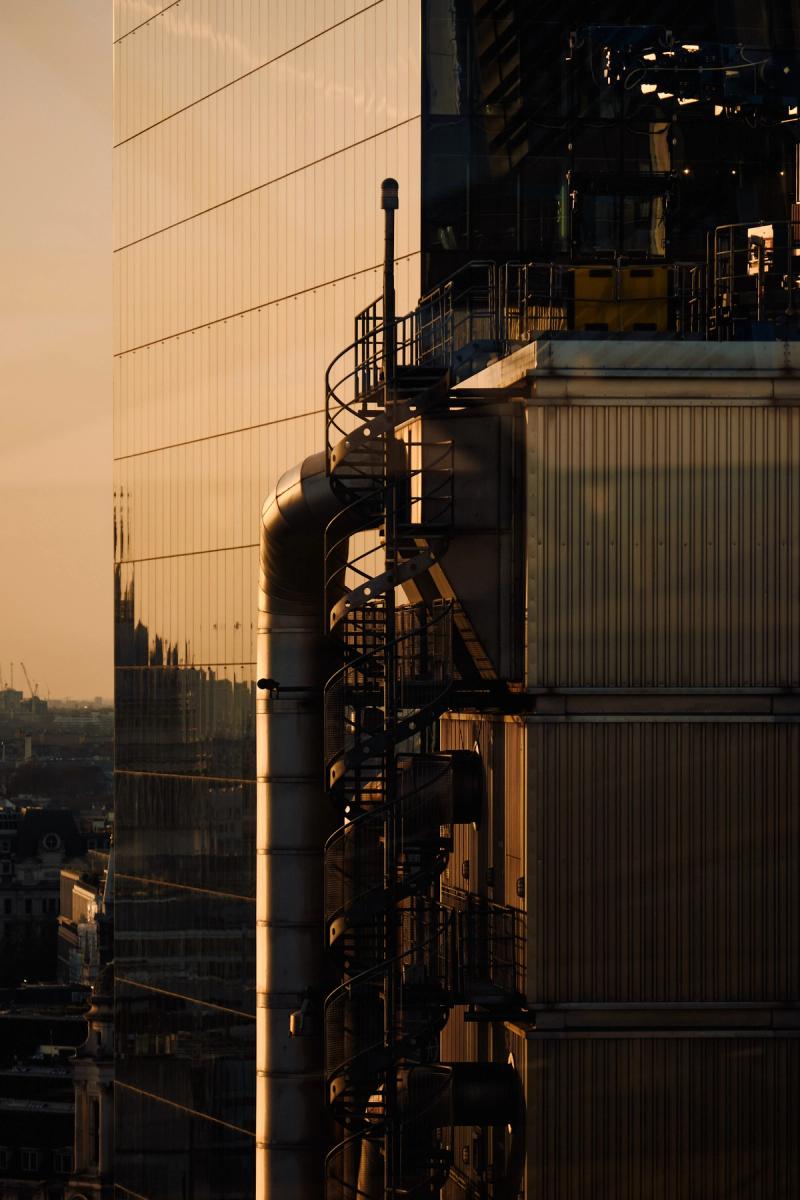 Industrial modern office building exterior at golden hour with corrugated metal cladding, spiral staircase and ventilation pipes, London cityscape