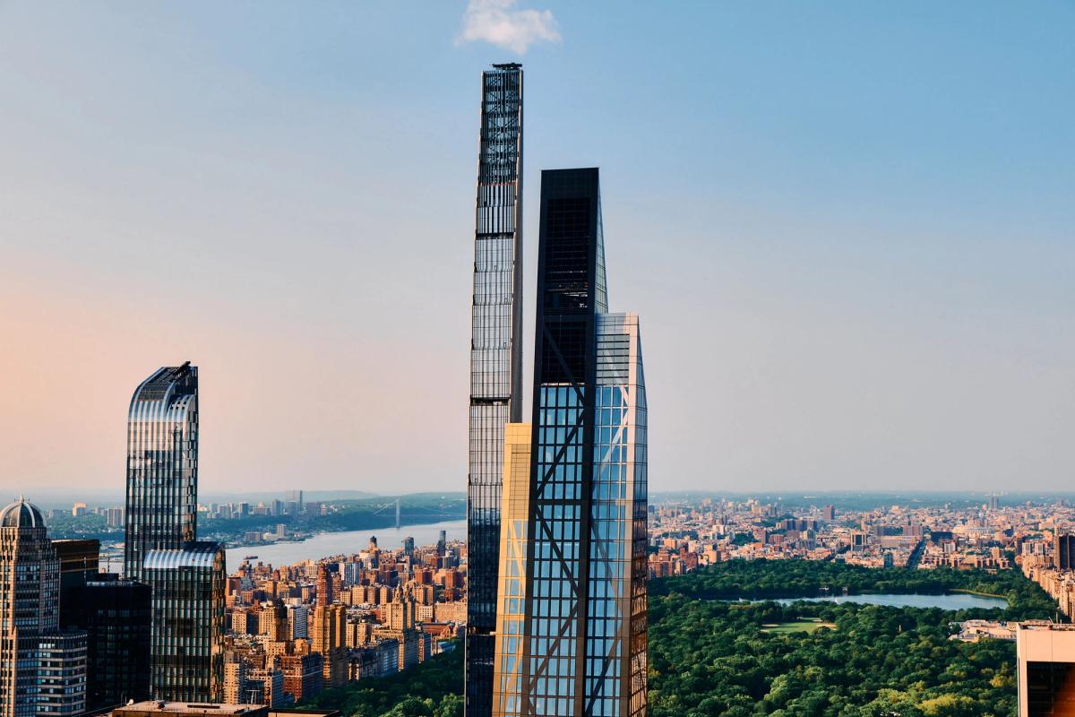 Modern asymmetrical high-rise tower with blue glass curtain wall and terracotta brick facade topped with antenna spire at golden hour sunset
