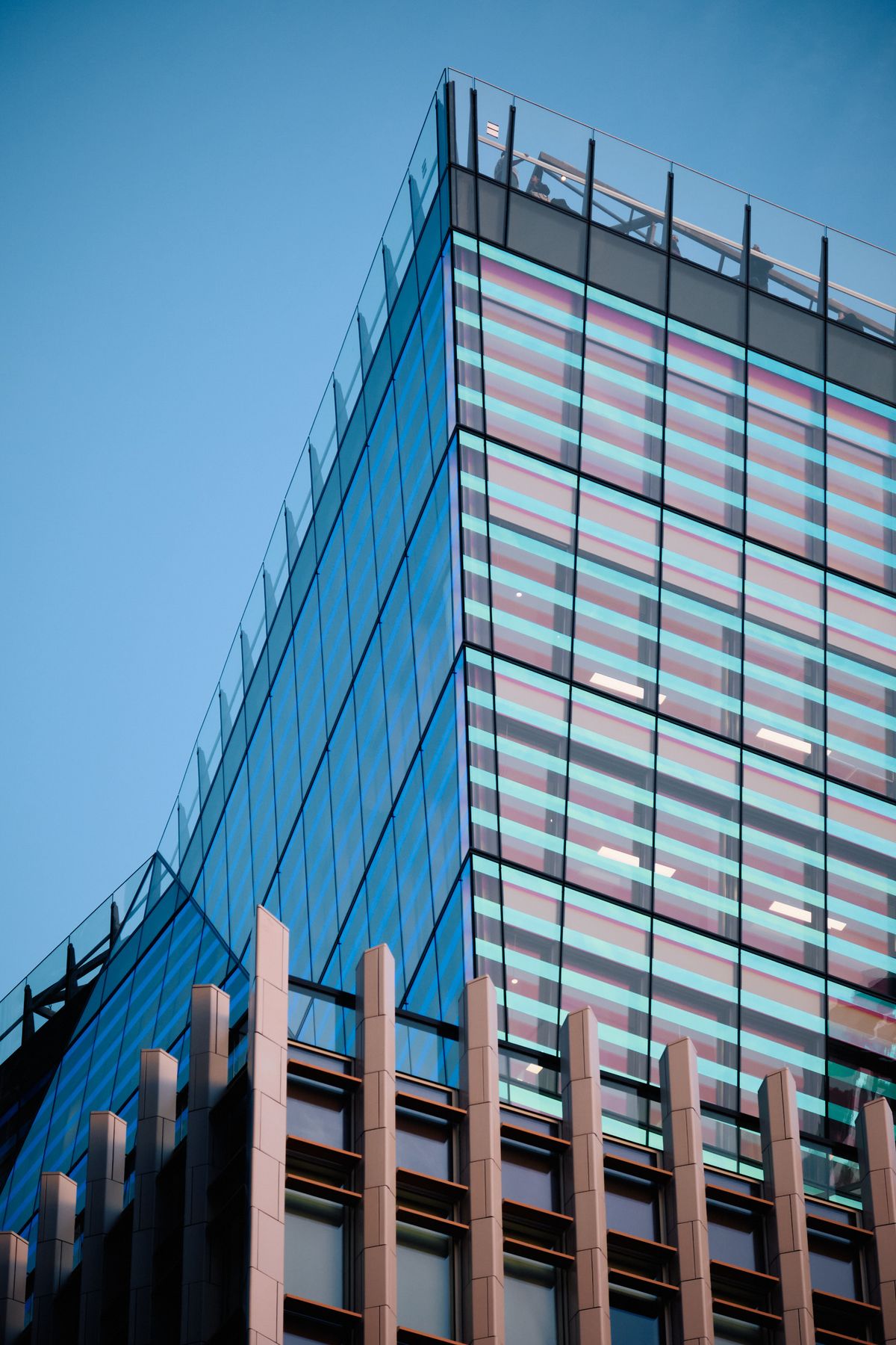Modern glass elevator shaft with blue interior lighting between contemporary building facades at dusk, urban architectural photography