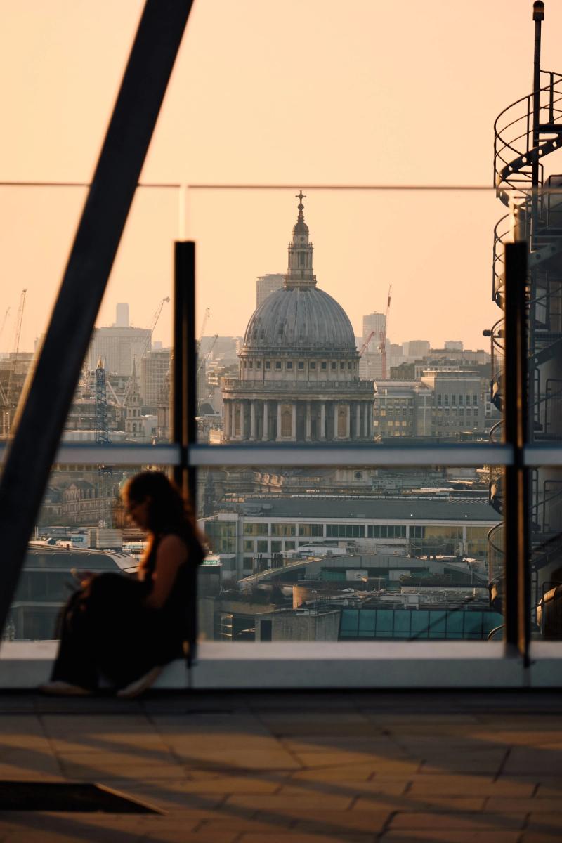 St. Paul's Cathedral London framed through modern glass railings from rooftop terrace at golden hour sunset, City of London skyline