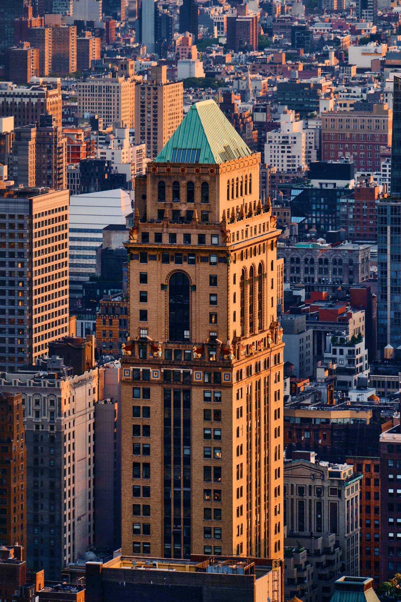 A cityscape with a tall, ornate clock tower in the center, surrounded by other buildings and a few cars.