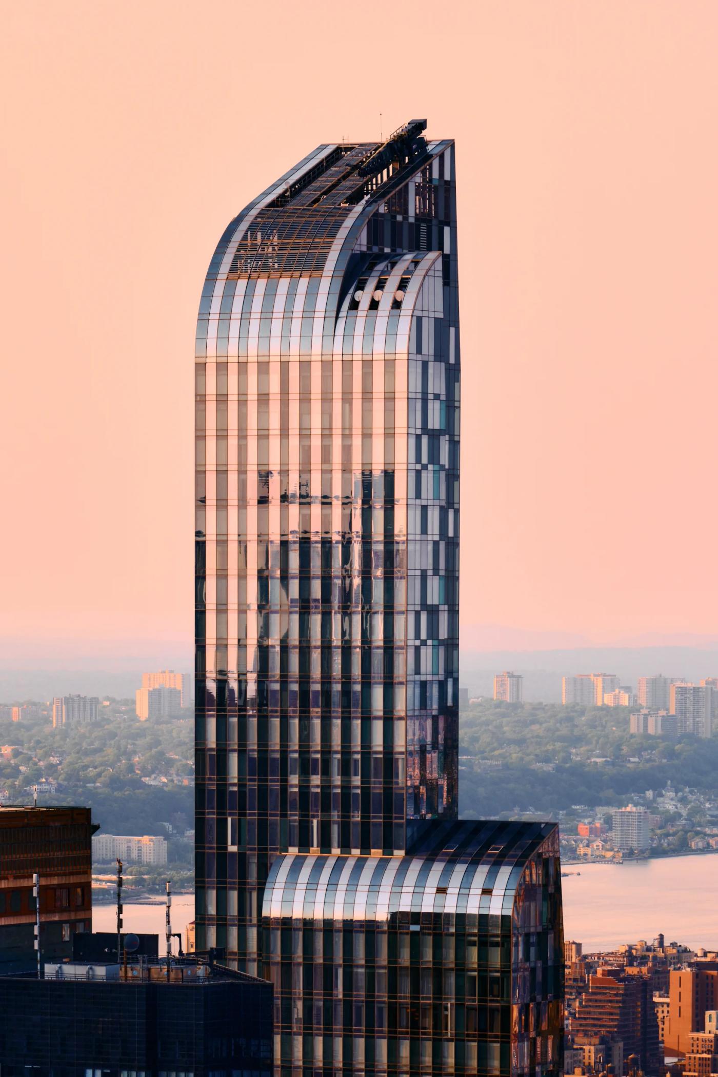 A modern skyscraper with a curved facade and reflective glass facade stands tall in a bustling cityscape, surrounded by other buildings and a body of 