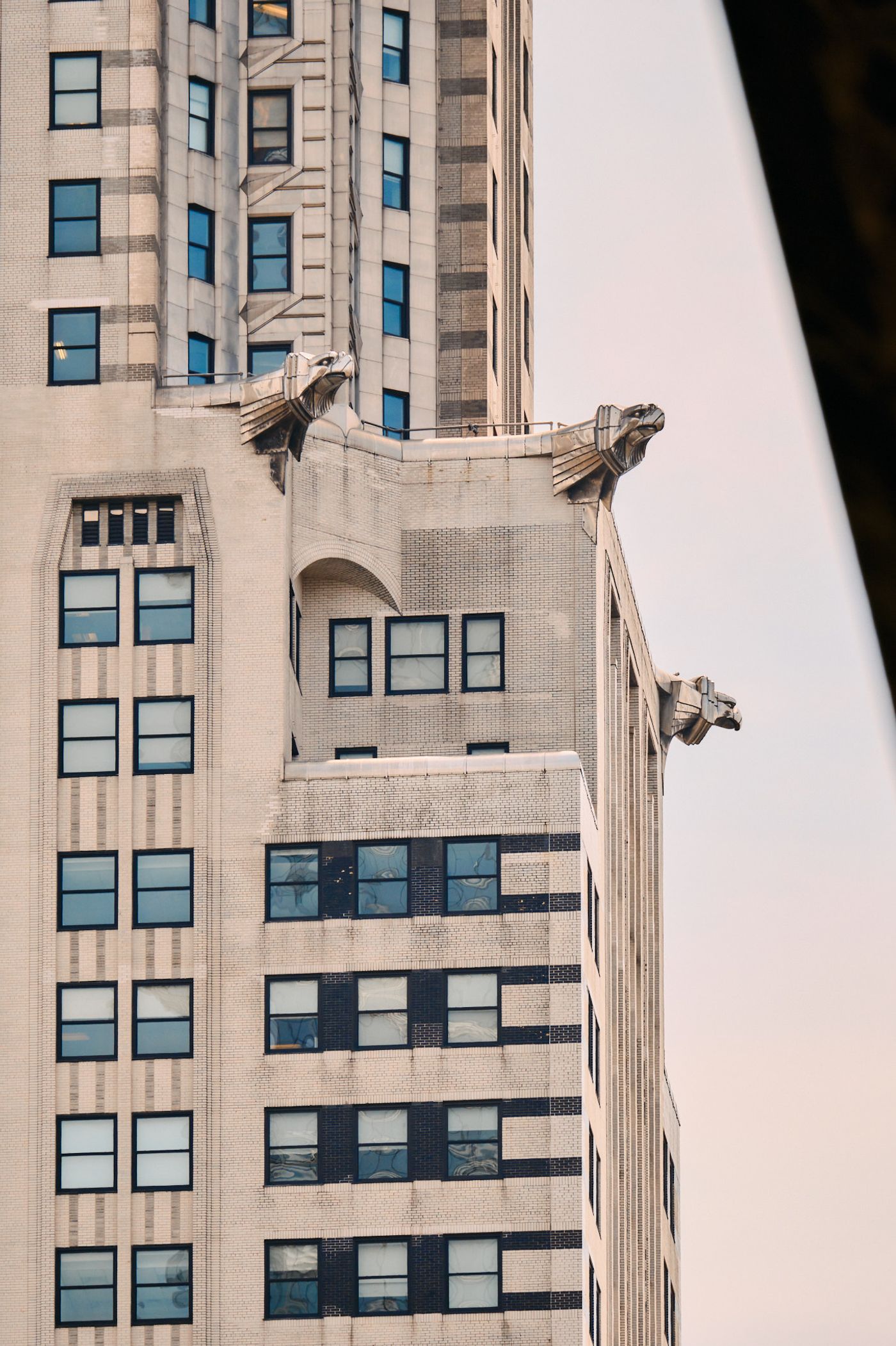 A tall, beige building with multiple windows and gargoyle-style windows on the roof is captured in the image. The gargoyle-style windows have wings an