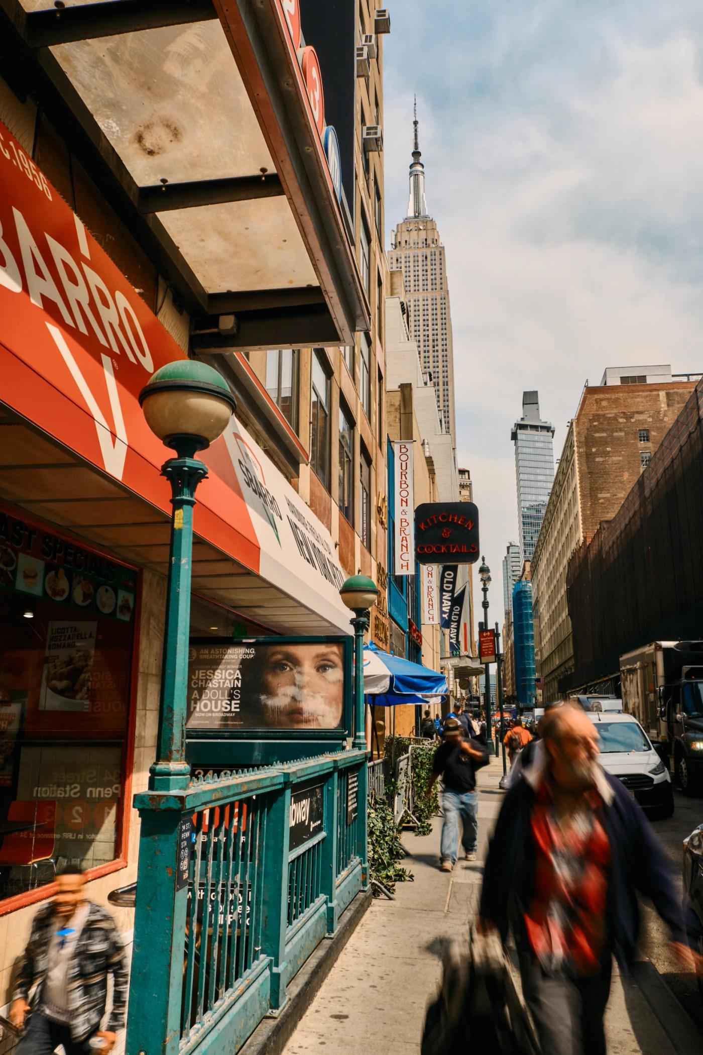 A bustling New York City street is filled with people, shops, and restaurants, with the Empire State Building towering in the background.