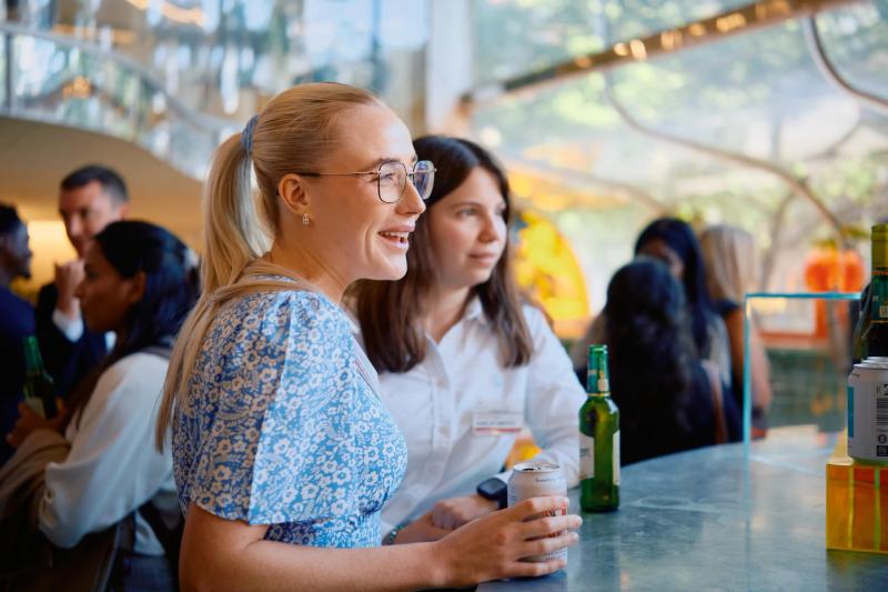 Two women sitting at a bar, one with glasses, the other with a beer.