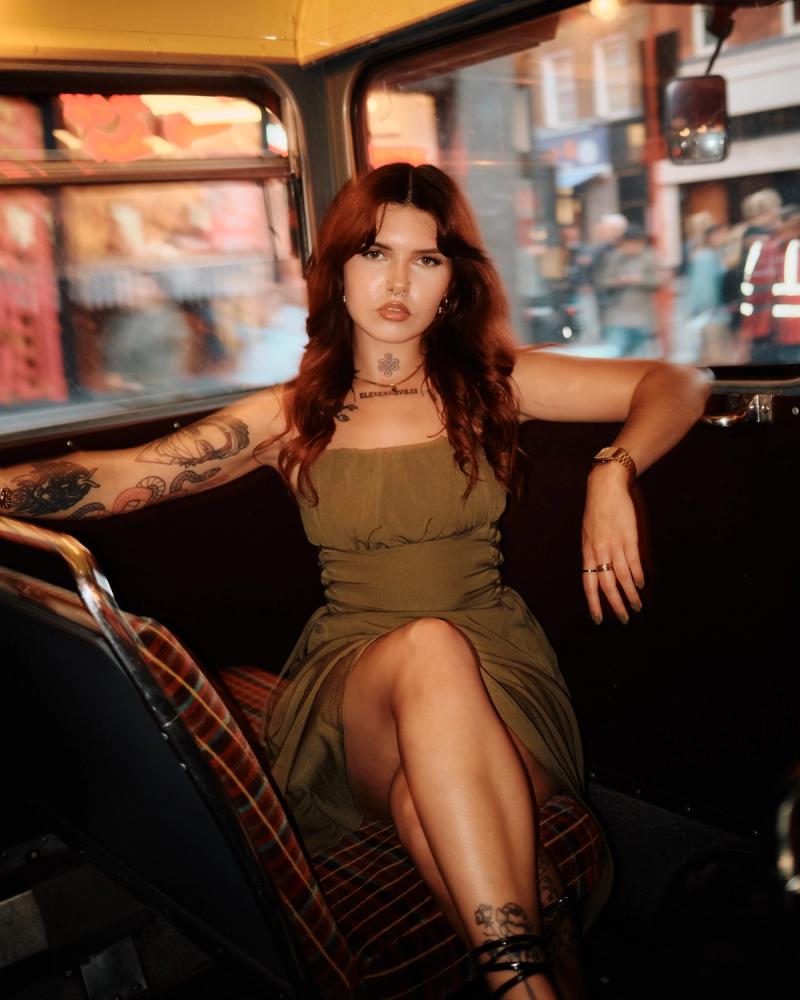 Tattooed woman lounging in a retro red booth under warm ambient light