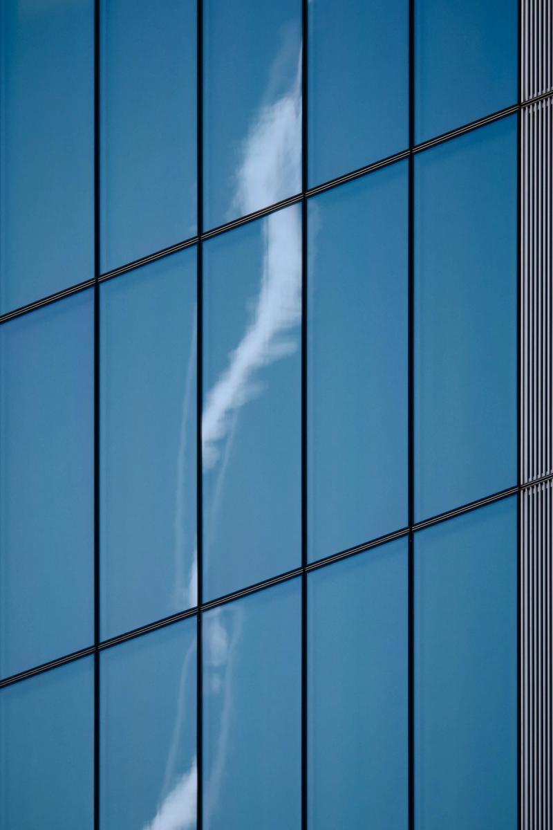 Modern commercial office building with reflective blue glass curtain wall and diagonal horizontal metal railings, minimalist architecture