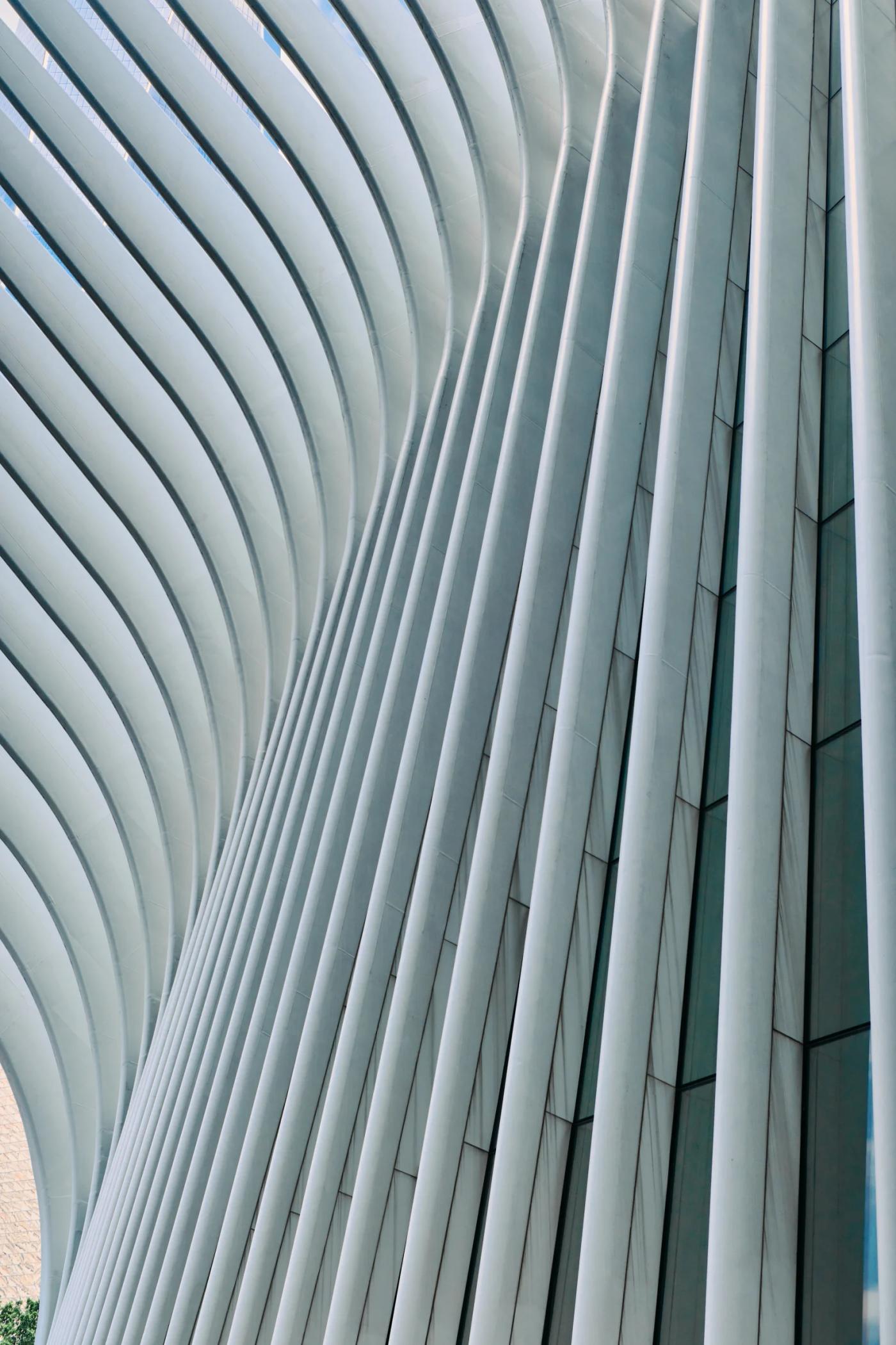 A modern, curved building with white, curved panels and a large glass window is captured in a close-up image. A person stands on the sidewalk in front