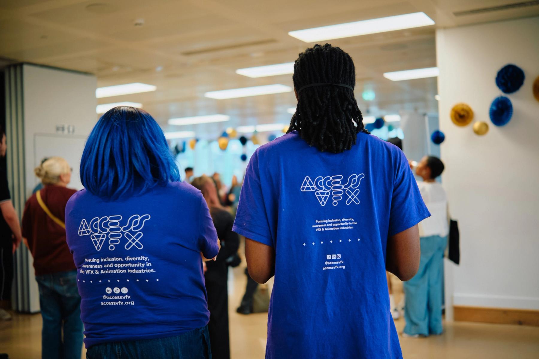 Access VFX community event 2026, two volunteers seen from behind in blue ACCESS VFX t-shirts facing the crowd