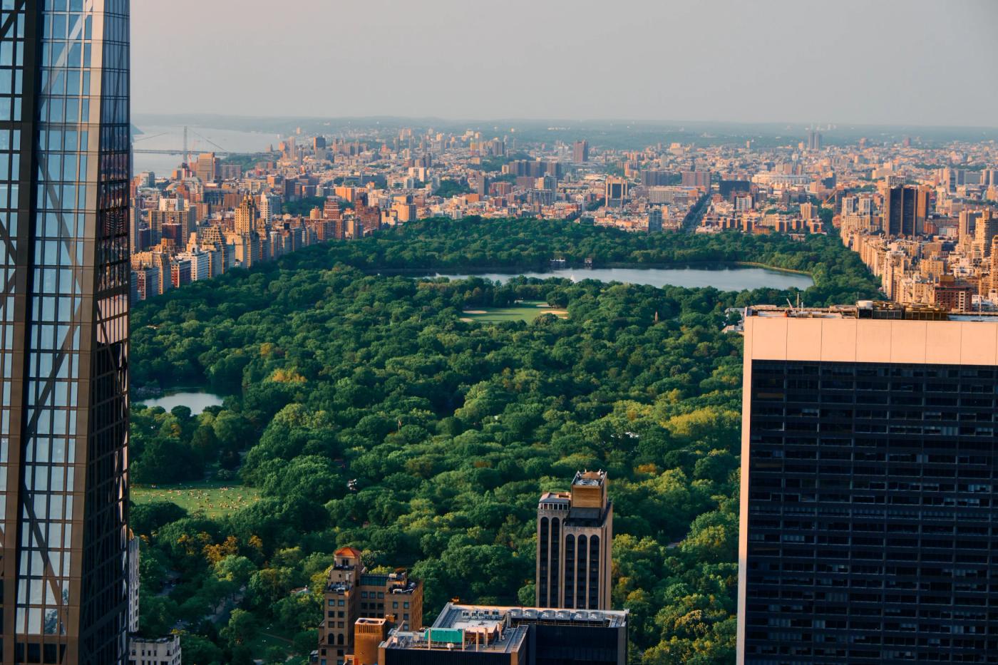 A panoramic view of New York City's iconic Central Park, surrounded by towering skyscrapers and a serene lake.