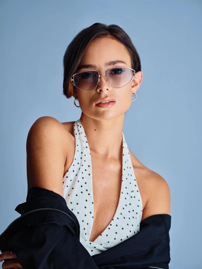 Fashion portrait of a woman posing with one arm raised against a clean blue background
