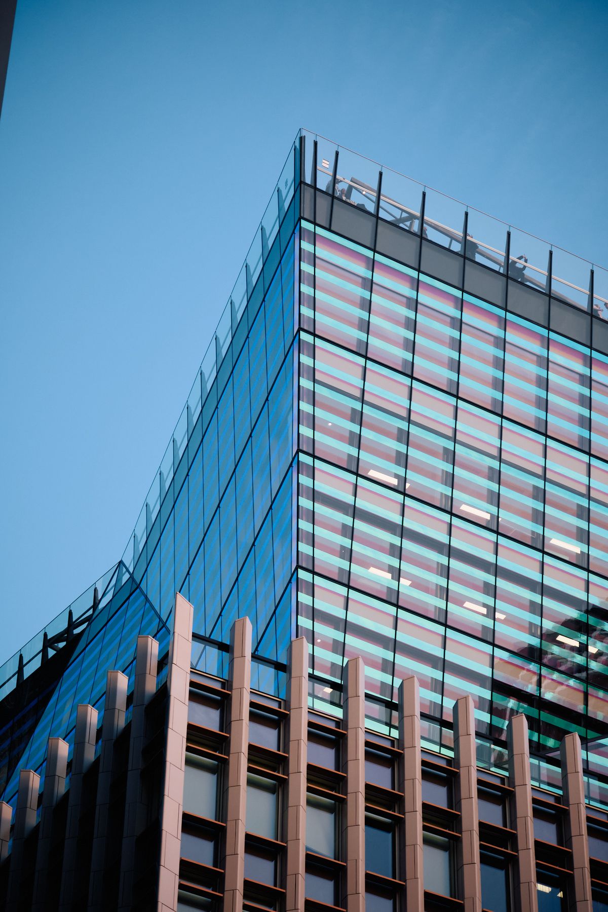 Modern glass elevator shaft with construction workers on illuminated platform and blue safety lights at twilight, contemporary urban architecture