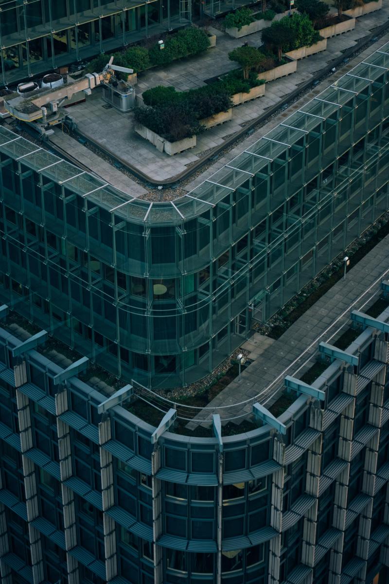 Aerial view of modern glass and steel office building complex with curved corner architecture and green rooftop terrace, London