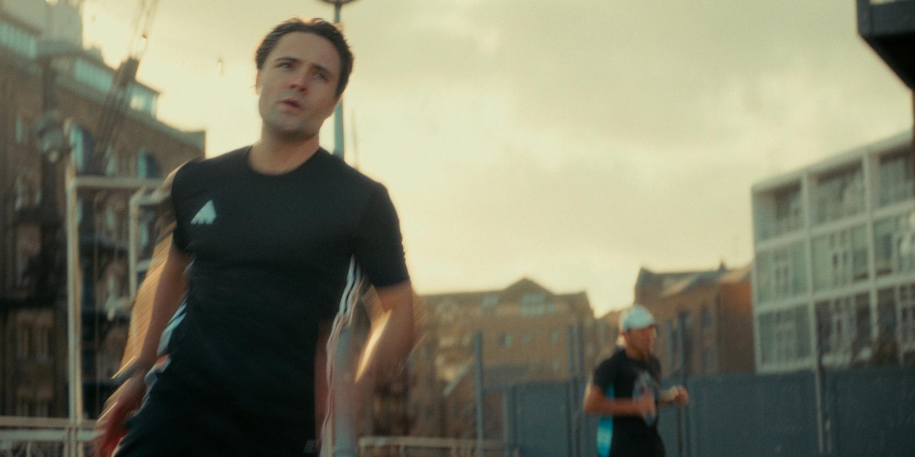 Man in black shirt and white cap, running on a street with buildings in the background.