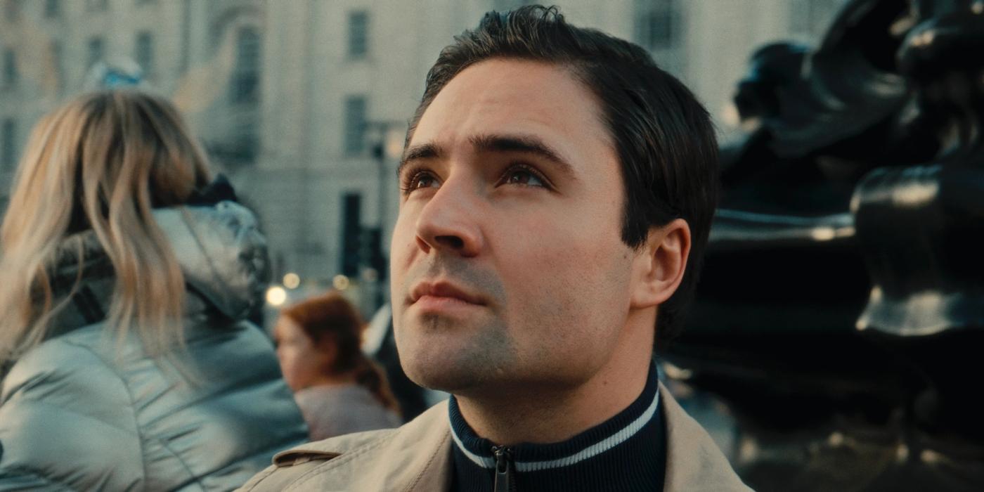 A man in a beige jacket gazes upwards, lost in thought, in a bustling city.