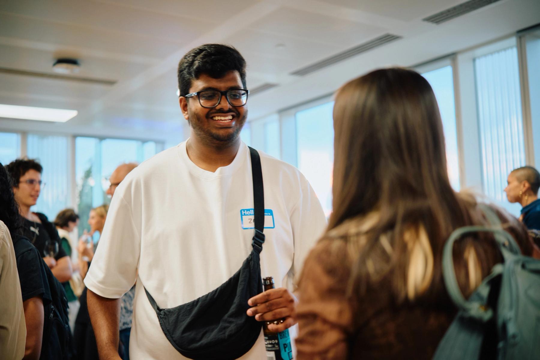 Access VFX community event 2026, smiling man in a white shirt and Hello name tag holding a bottle while chatting