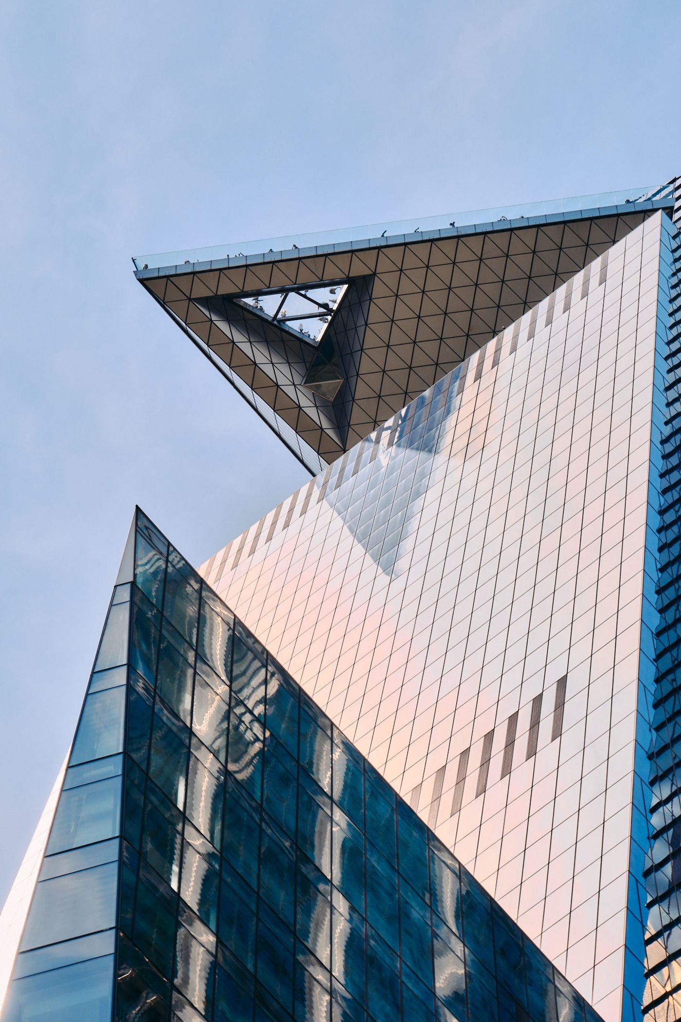 A modern, glass and steel building with a triangular top and a large metal beam is captured in a low-angle shot, showcasing its unique design and arch