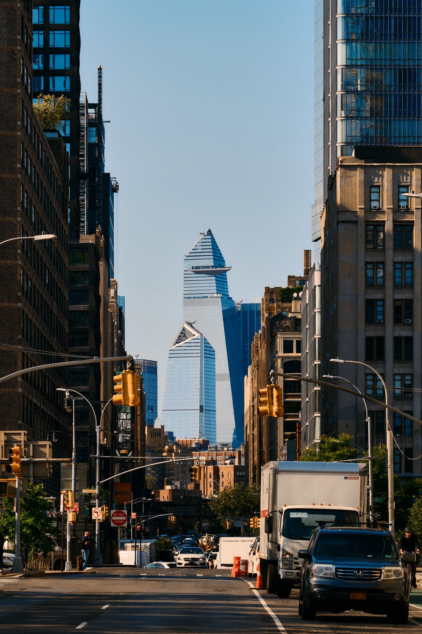 A bustling New York City street is captured from a low angle, showcasing towering skyscrapers, traffic lights, and a truck.