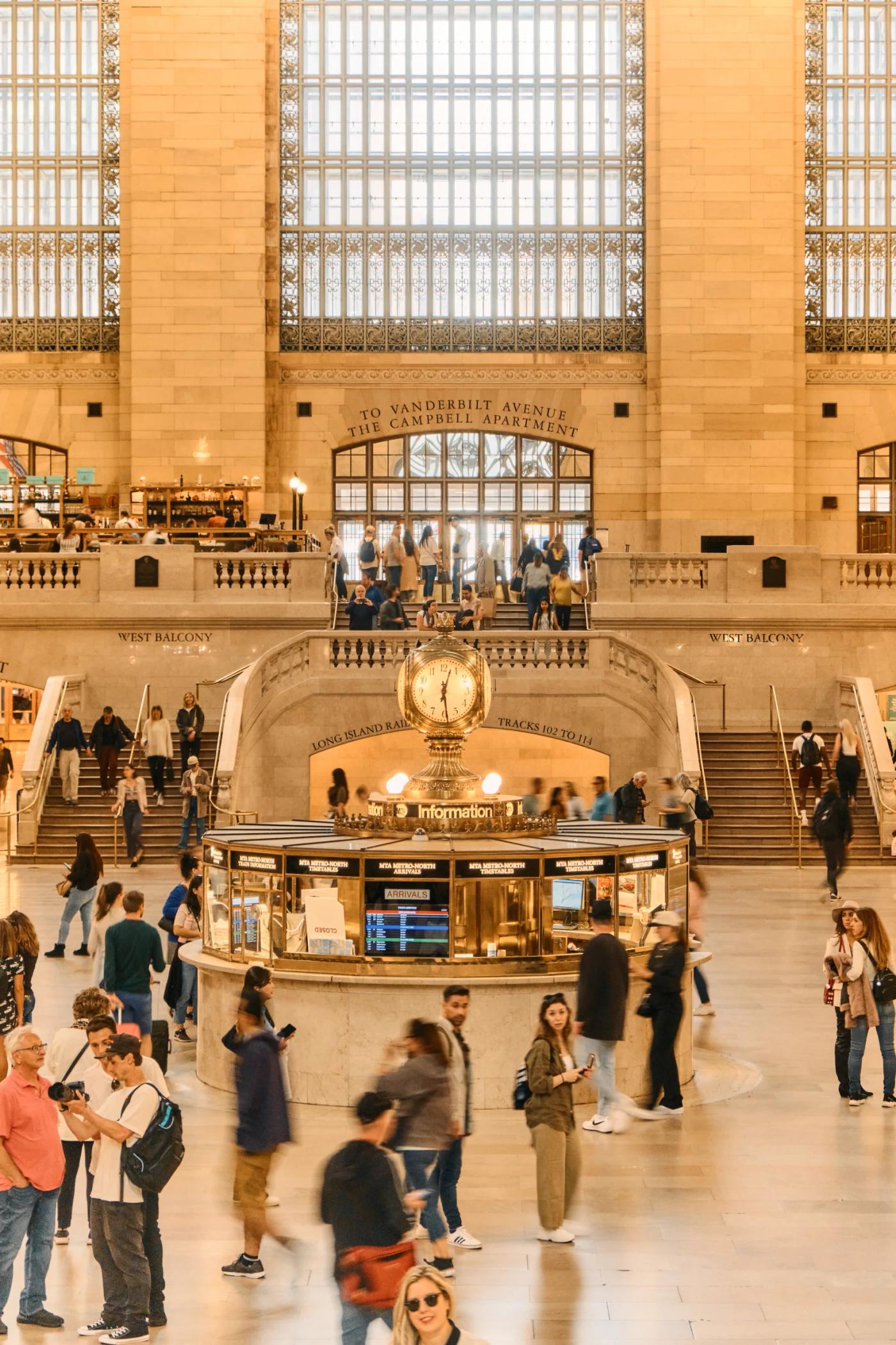 The image captures the bustling scene at the New York Central Station, with a grand architecture and a large chandelier hanging from the ceiling. The 