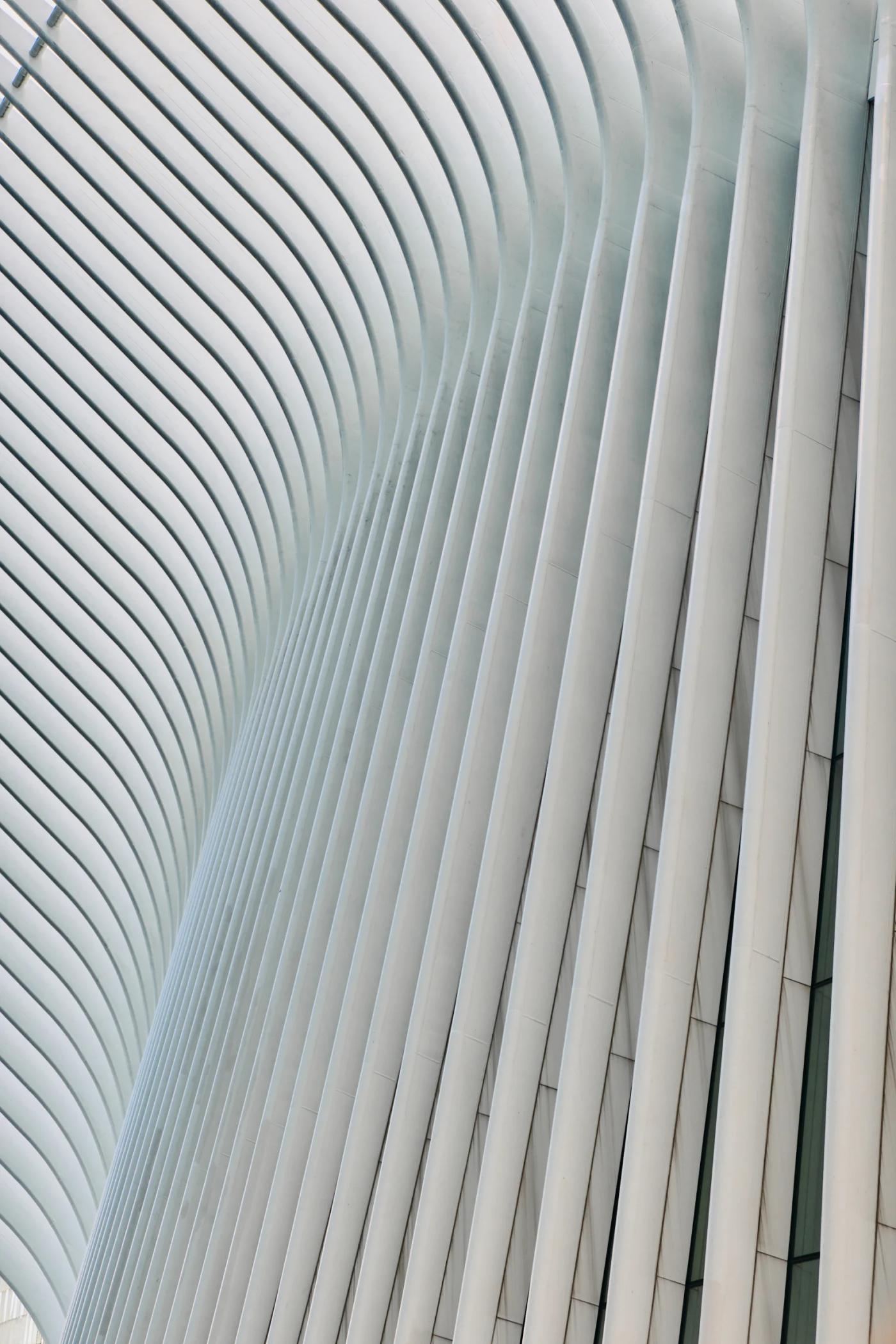 A modern, curved building with white, curved panels, a person standing in front, and a clock on the side.