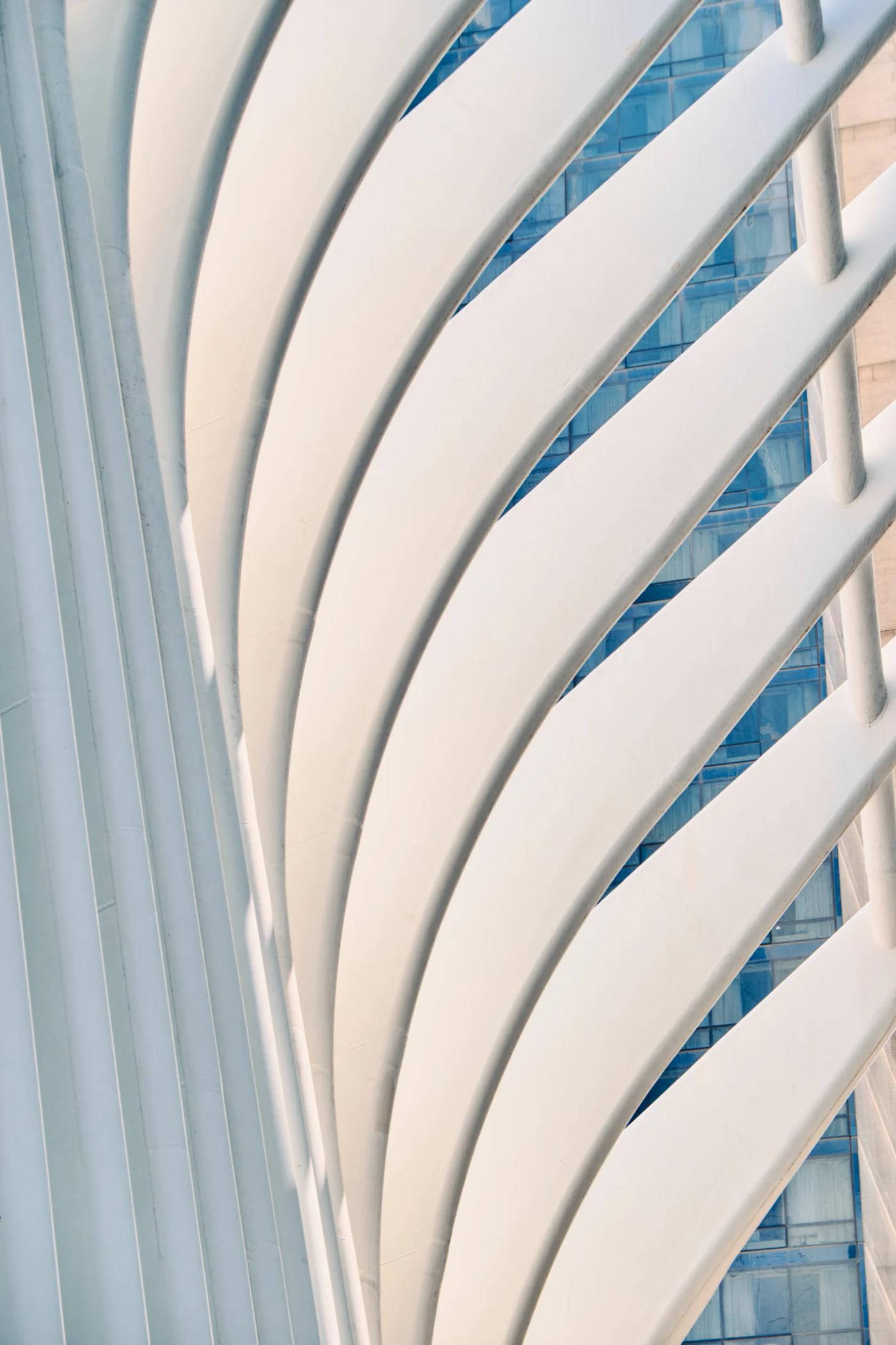 A modern, white, curved structure with a blue glass facade stands in front of a tall, modern building.