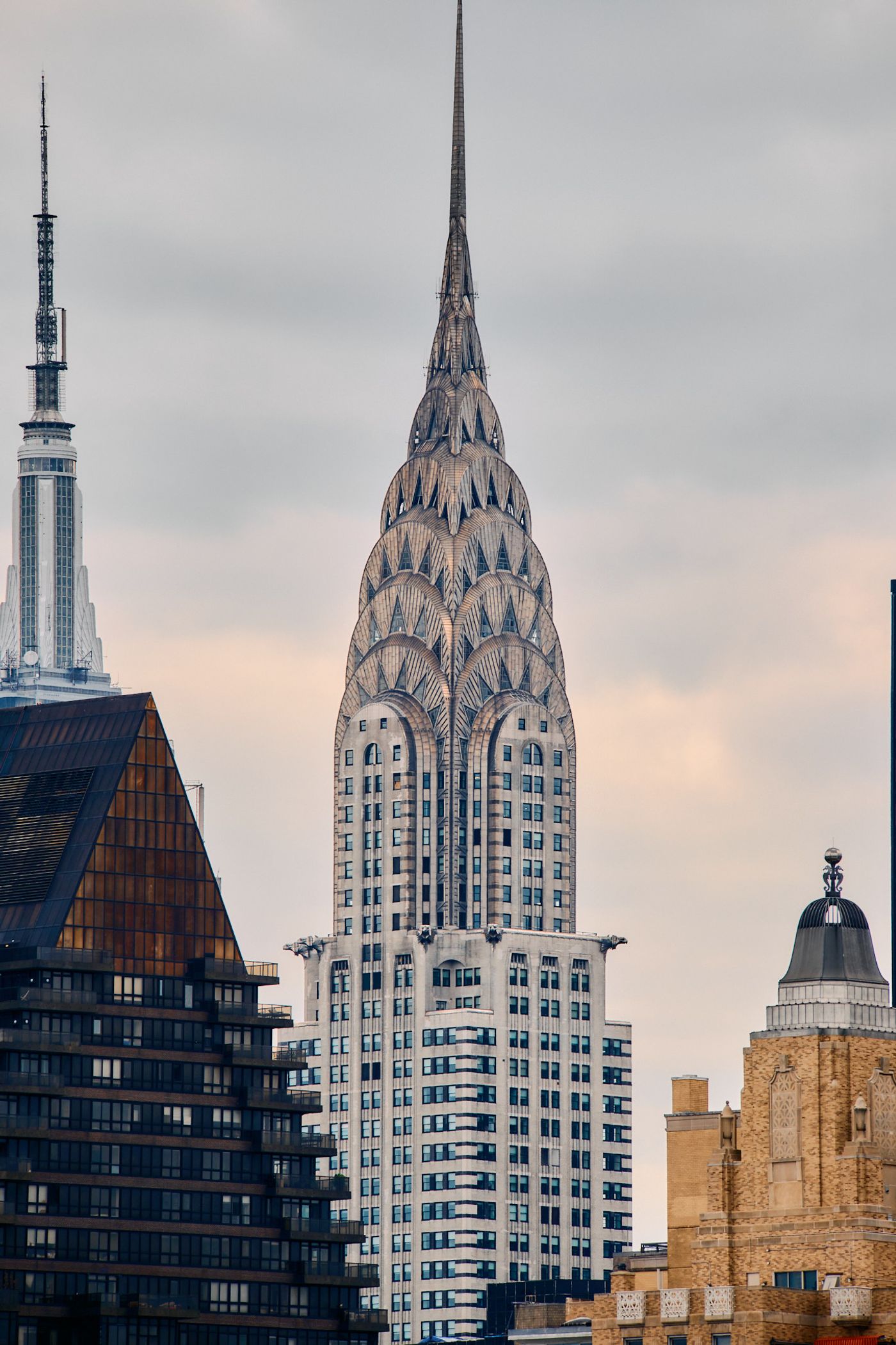 The Empire State Building, a white, glass skyscraper with a pointed spire, stands tall in New York City, surrounded by other buildings and a cloudy sk