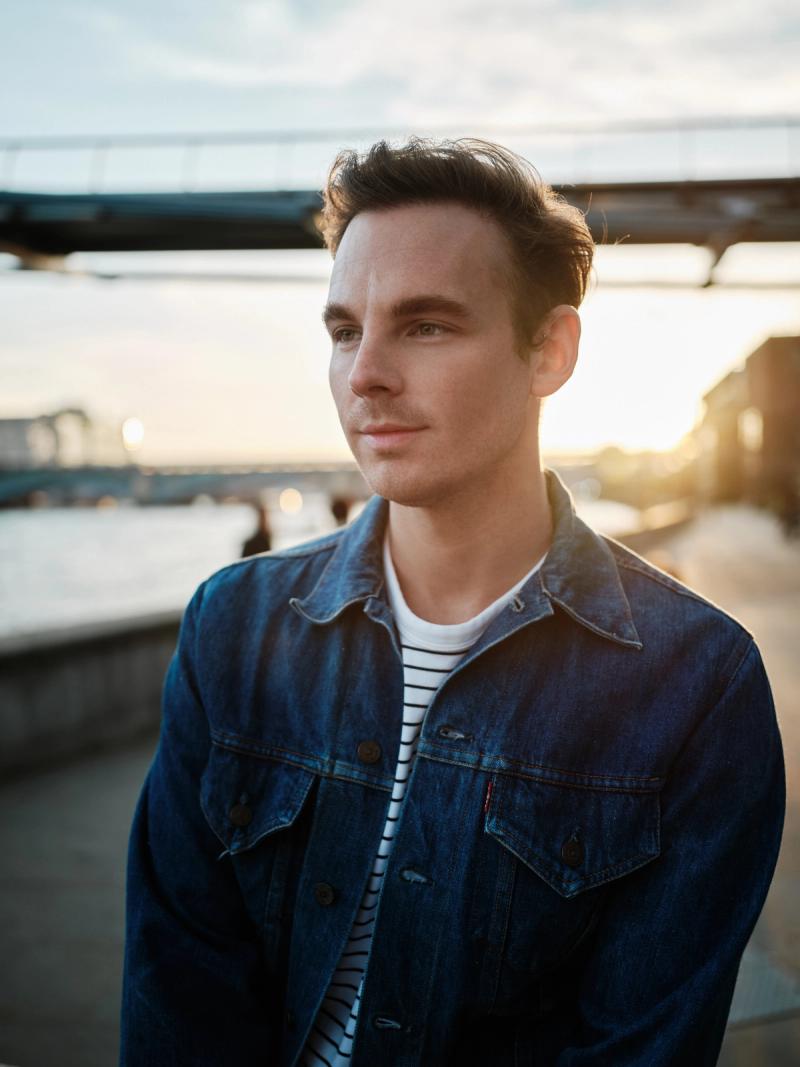 Male portrait in denim jacket with soft sunset light near a riverside railing