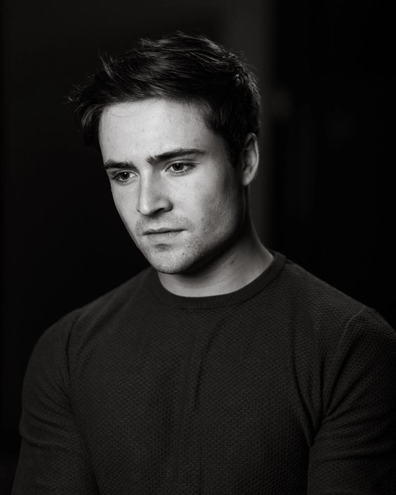 Black-and-white portrait of a man in a dark crewneck against a black background