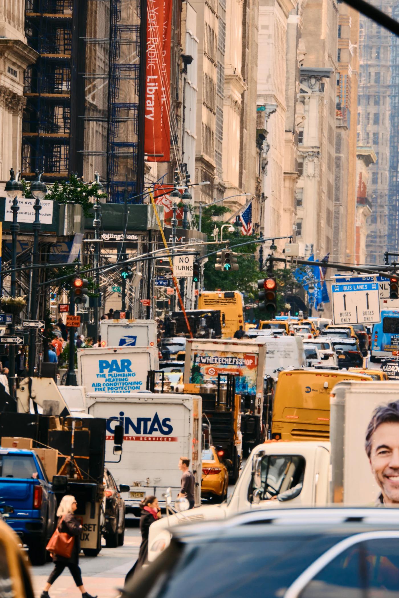 A bustling city street filled with various vehicles, including cars, trucks, and buses, surrounded by tall buildings and adorned with banners and sign