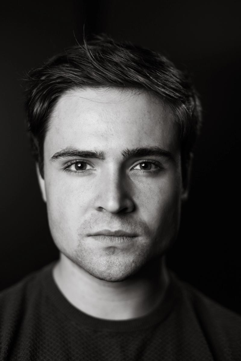 Close black-and-white headshot of a man with a neutral expression