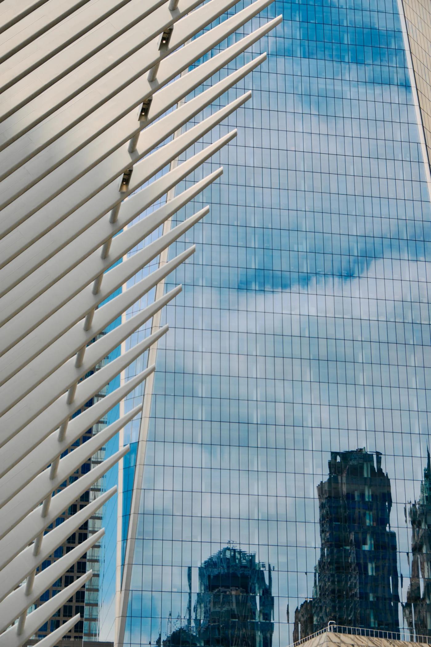 A modern skyscraper with a blue glass facade and white vertical lines is reflected in a clear blue sky, creating a striking contrast.