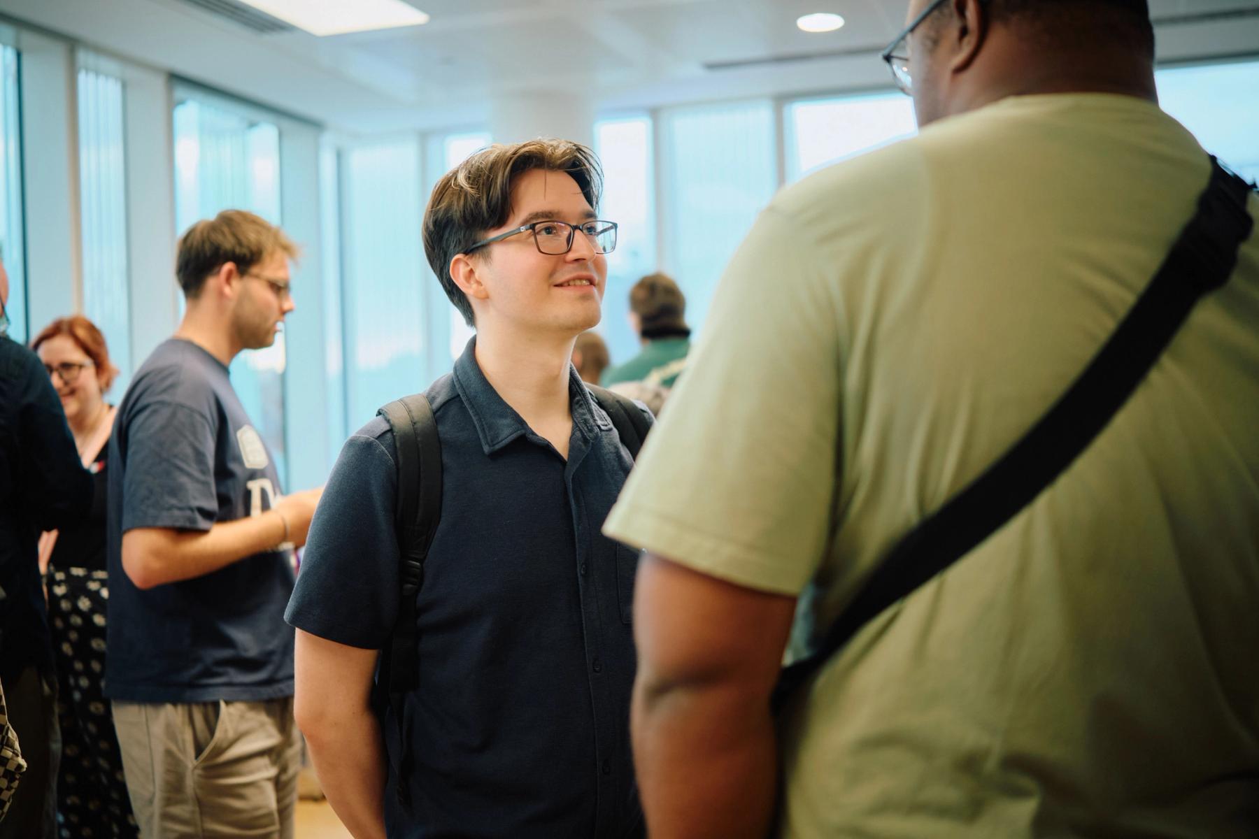 Access VFX community event 2026, young man in glasses and a blue shirt smiling mid-conversation by the windows