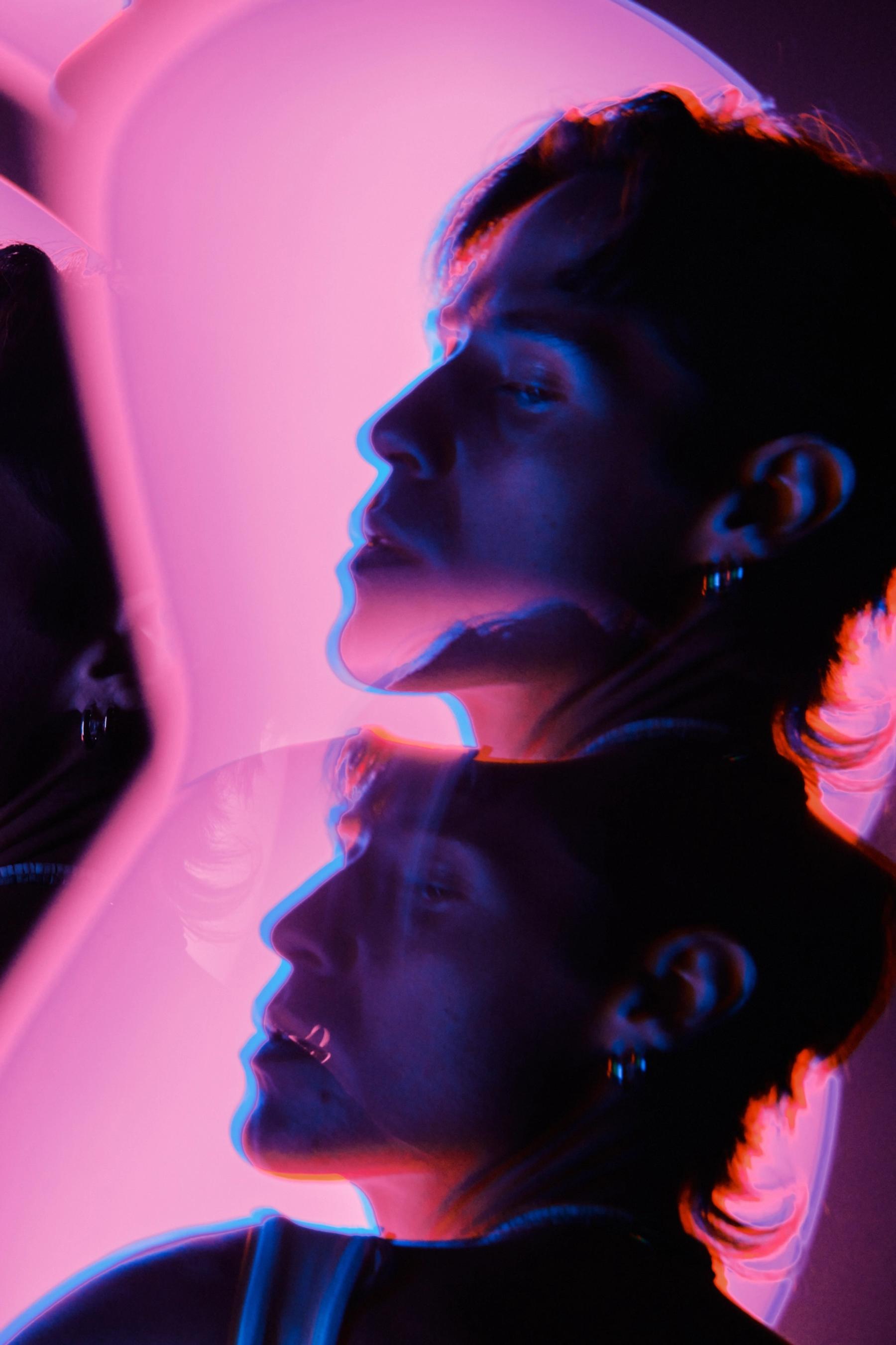 A woman with a pinkish hue, wearing earrings, is reflected in a mirror, with her face and hair in multiple perspectives.