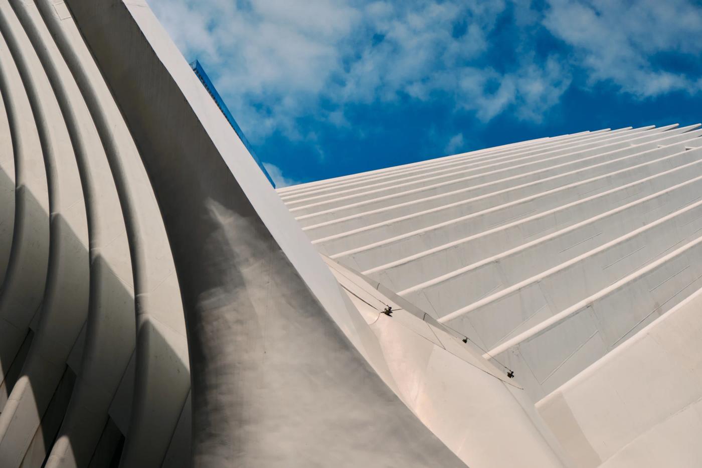 A modern, white, curved building with a blue sky backdrop is captured in a low-angle shot, emphasizing its architectural details.