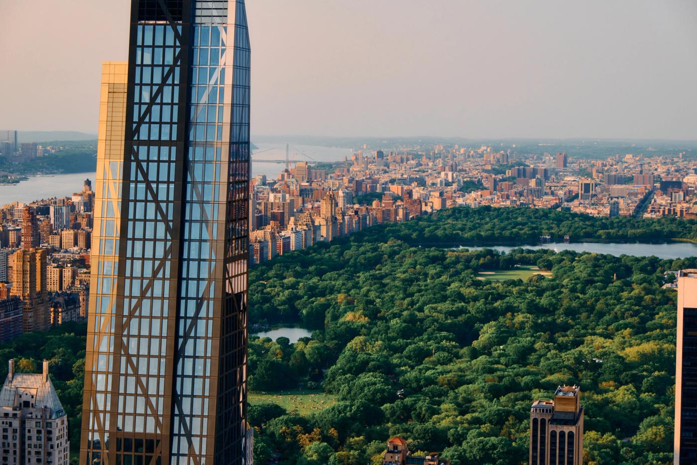 A skyscraper with a glass facade and blue tint dominates the left side of the image, surrounded by a lush park and a city skyline.